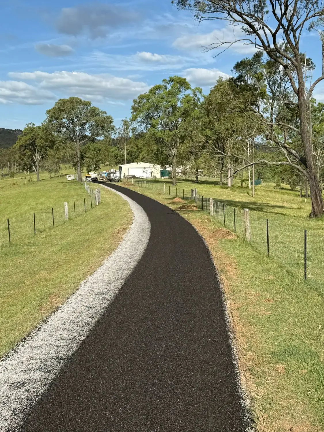 Sealed rural driveway with gravel edging through a grassy field.