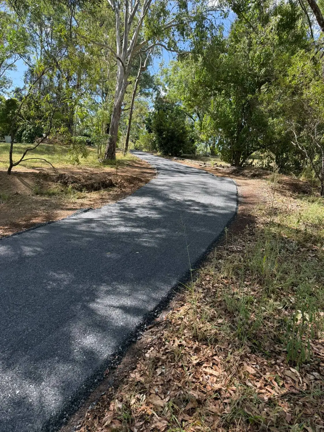 A newly paved asphalt driveway winding through a wooded bushland area